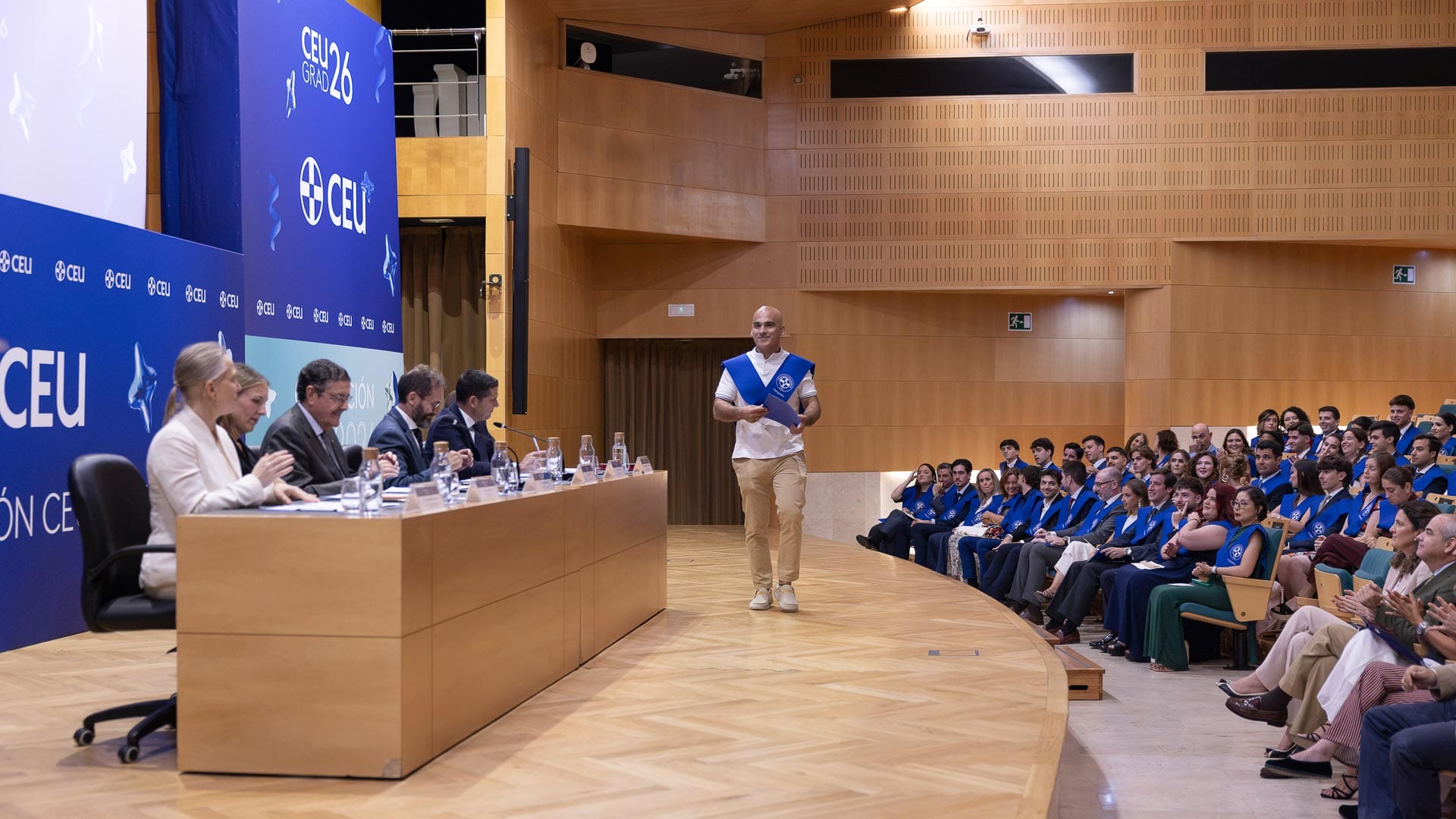 Alumno graduado de máster en la CEU UF3 caminando hacia la mesa presidencial para dar su charla.