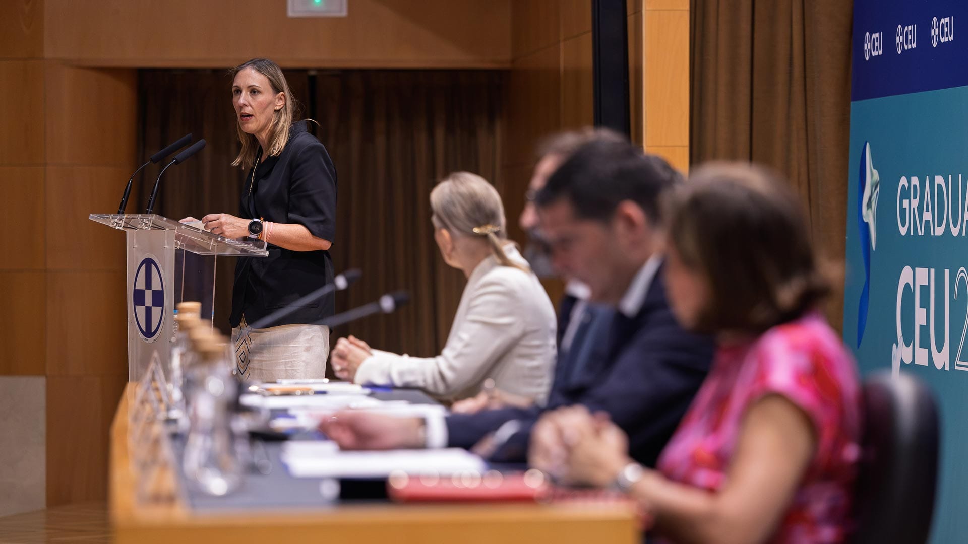 Lorena Garrido en el atril de la ceremonia de graduación de máster en la CEU UF3, con la mesa presidencial al fondo.
