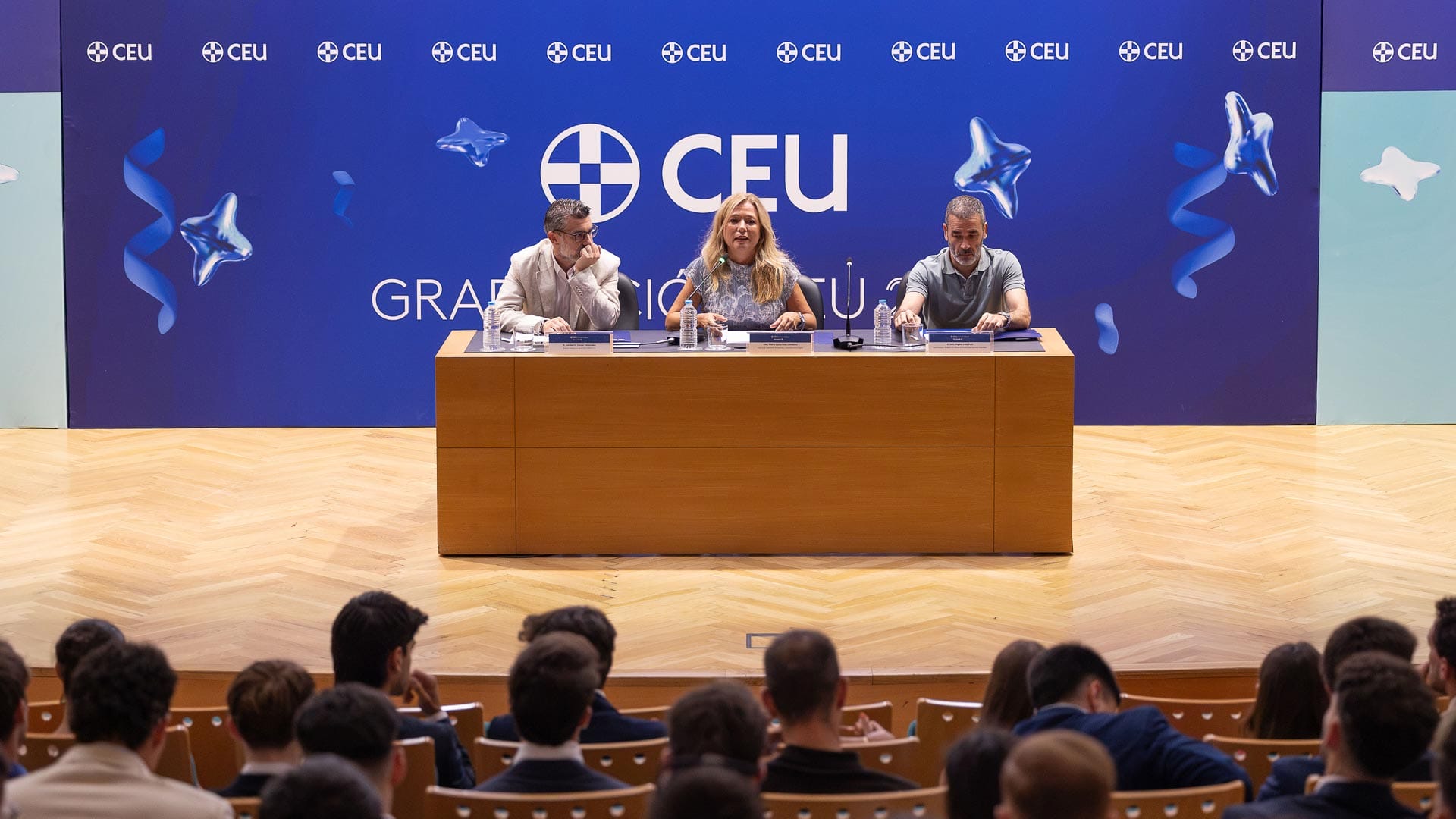Tres ponentes en una mesa con un gran fondo azul que dice "CEU" y "GRADUACIÓN", durante el acto de clausura de un máster en la CEU UF3.