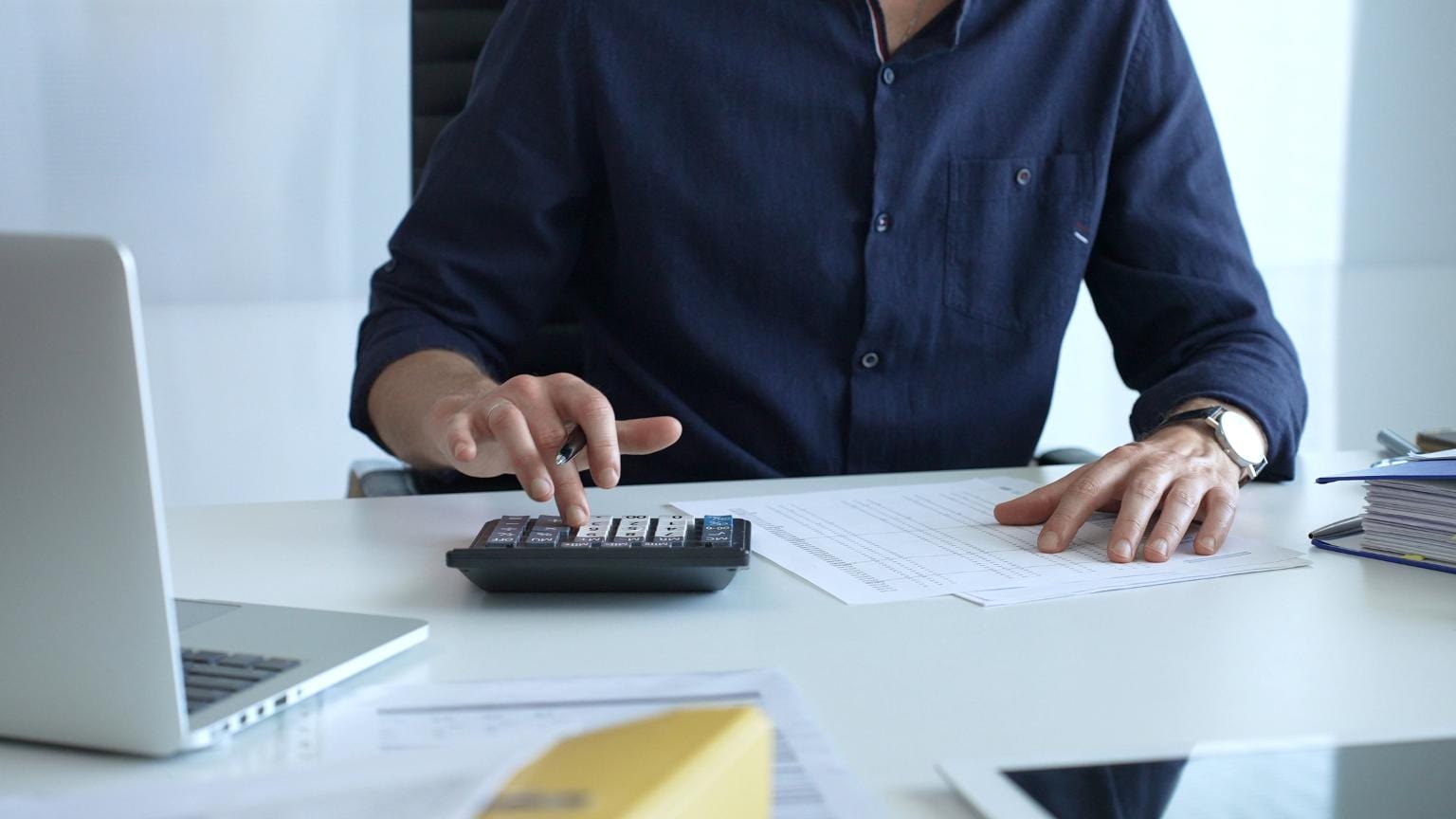 Auditor de cuentas realizando cálculos financieros y revisando balances con calculadora y documentación contable