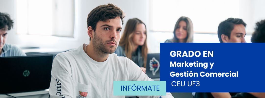 Alumnos del grado de Marketing y Gestión Comercial de CEU UF3 en Sevilla participan en una clase práctica, atentos a la explicación del profesor mientras toman apuntes y utilizan sus portátiles en un aula moderna.