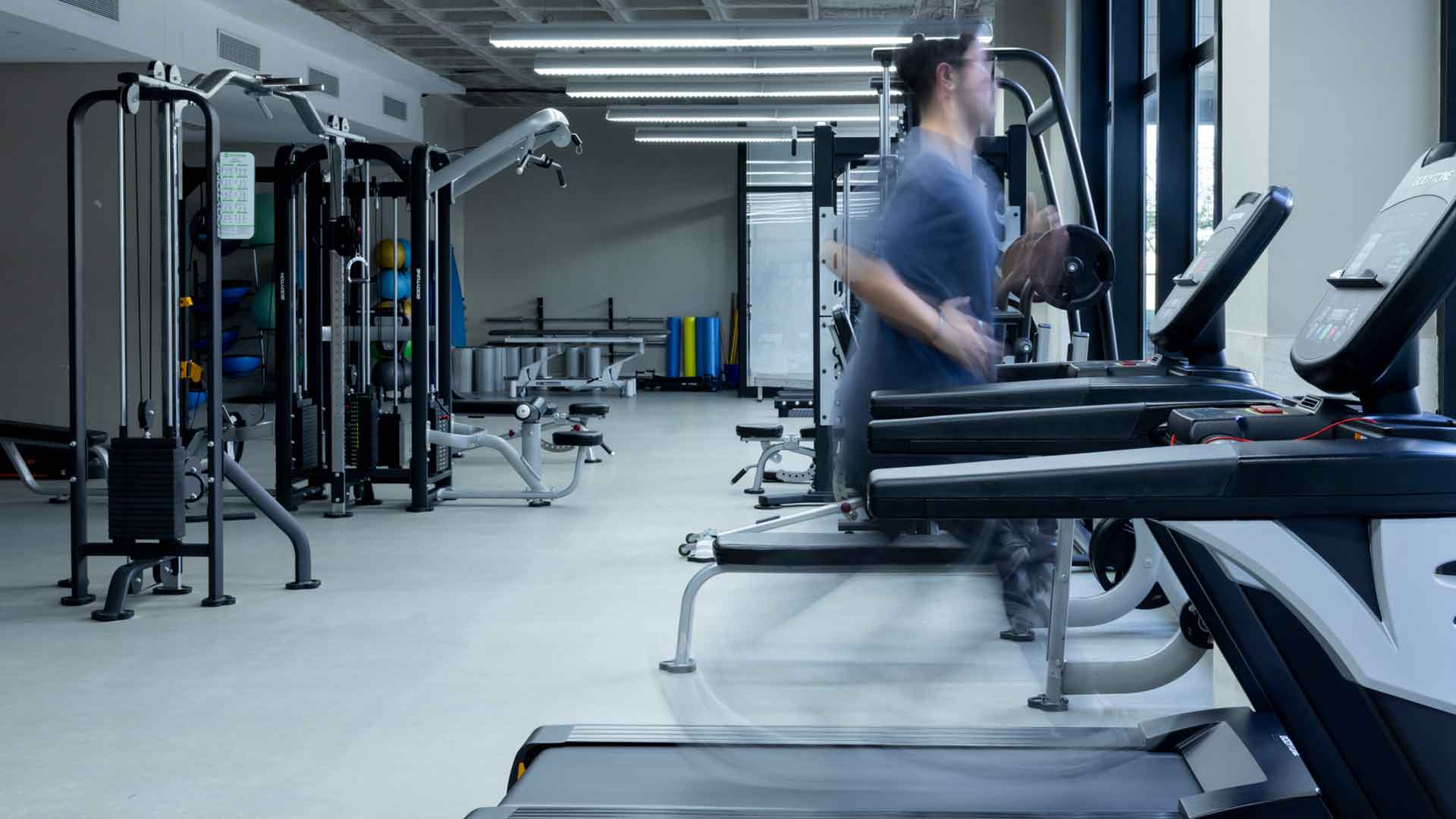 Estudiante de CAFyD en cinta de correr dentro del gimnasio y sala de musculacion equipada del campus de la Universidad CEU Fernando III en Bormujos.