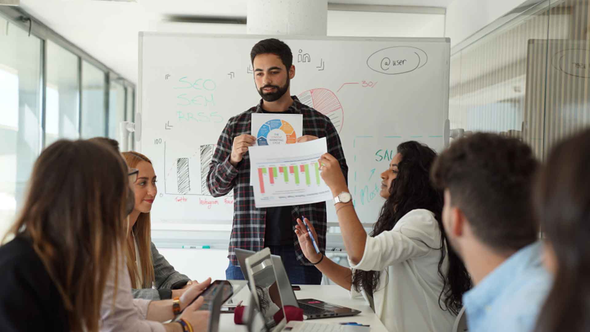 Jóvenes profesionales analizando gráficas en una reunión de trabajo sobre por qué estudiar marketing.